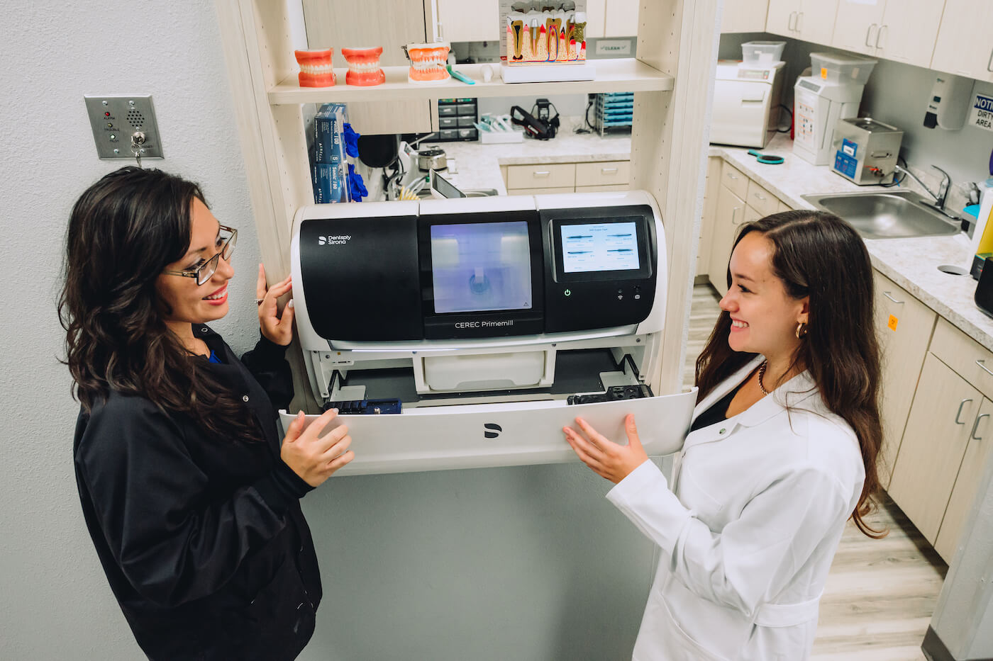 A new dentist works with her mentor, who is teaching her how to use the machinery in their dental practice.