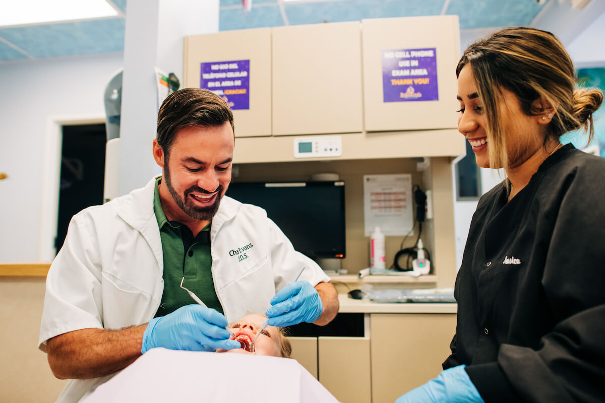 A dental hygienist watches over a dentist as he cleans a pediatric patients teeth in a dental service organization-owned practice.