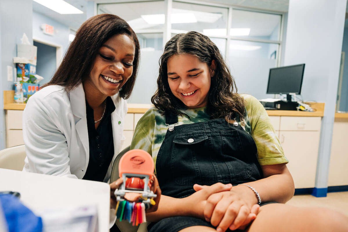 Dentist showing teen female a set of teeth. Your patients deserve to feel proud of their smiles.