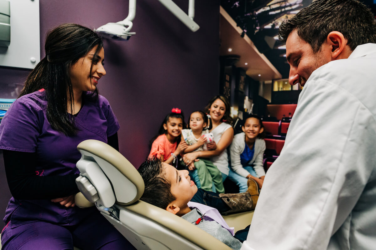 A dentist and hygienist speak with a pediatric patient while his family looks on.