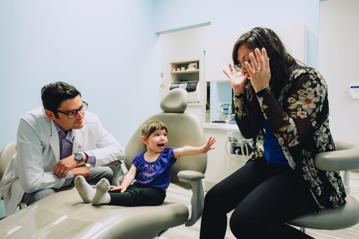 A dentist bonds with a pediatric patient while her mentee observes.