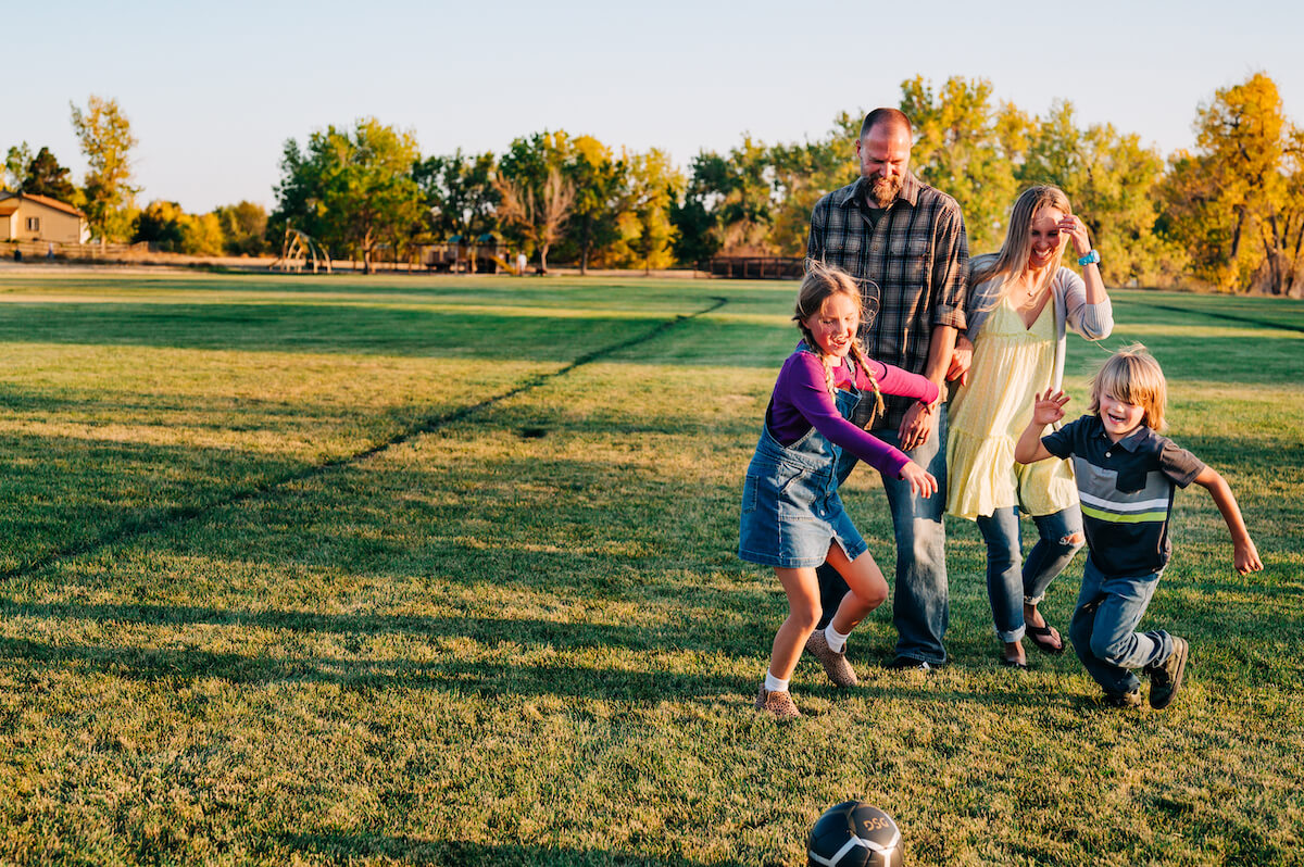 A dentist, her spouse, and their kids enjoy the outdoors on a weekend, playing soccer together in a park.