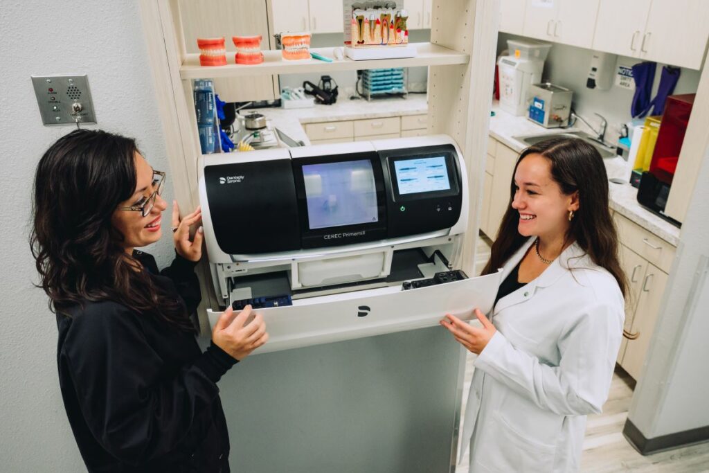 Two female dental professionals standing near a CEREC milling machine. 