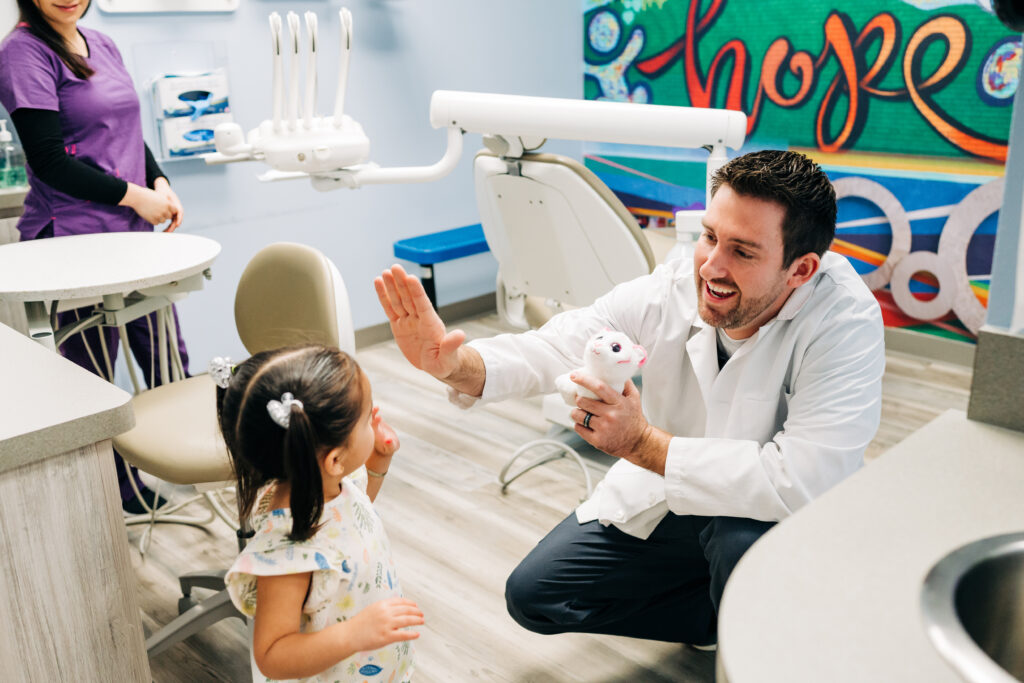 Family Smiles dentist giving young female child a high five. Working with children is one of many soft skills needed to be a dentist.