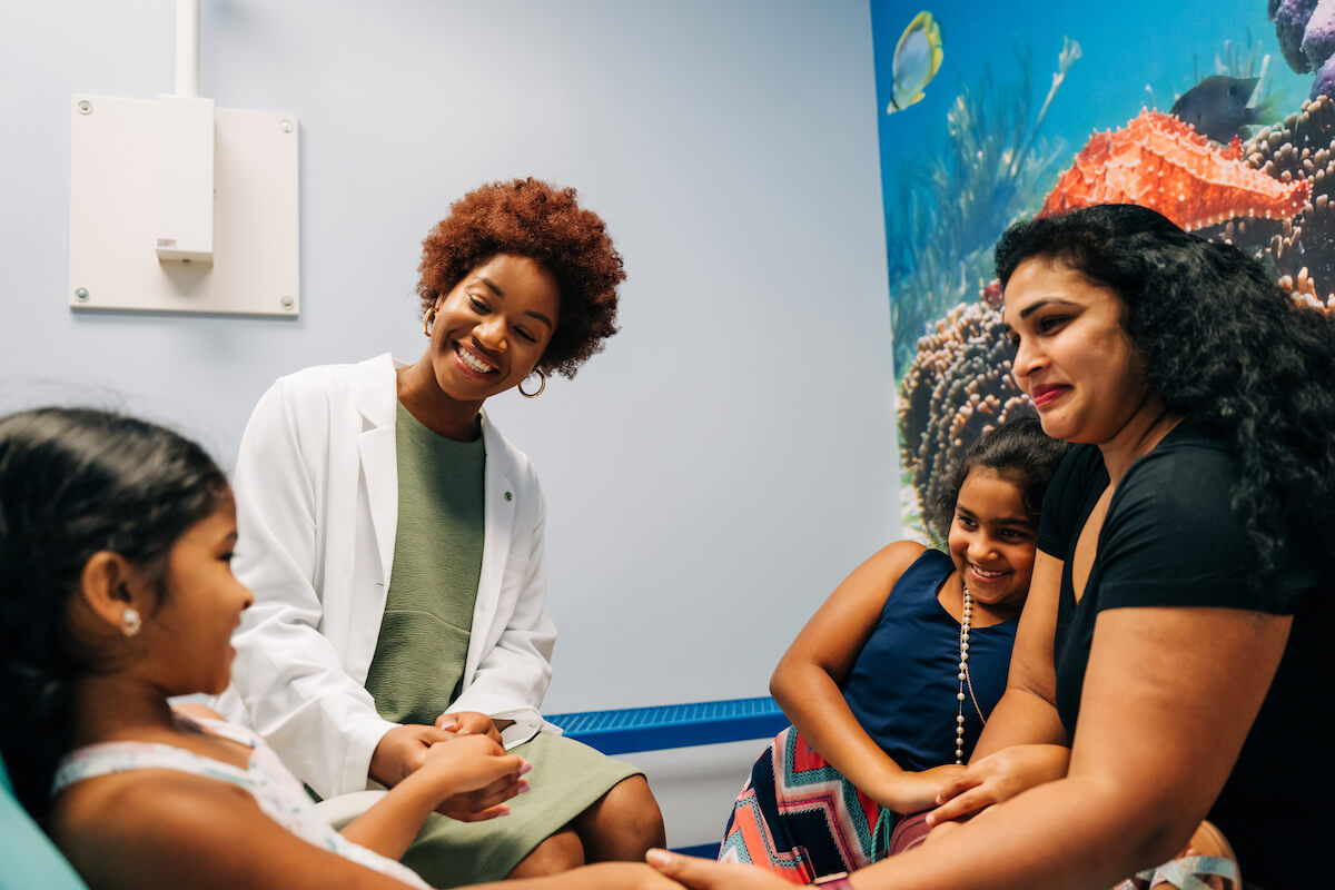 A new dentist sits with a pediatric patient and her family during a checkup.