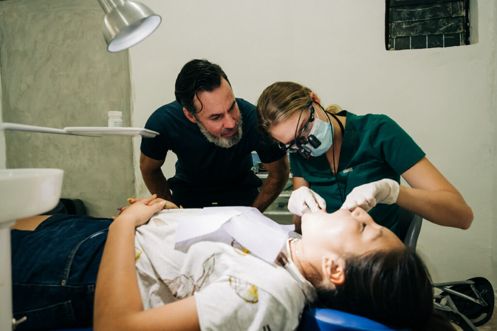 Dentist and dental assistant look inside a young female's mouth. 
