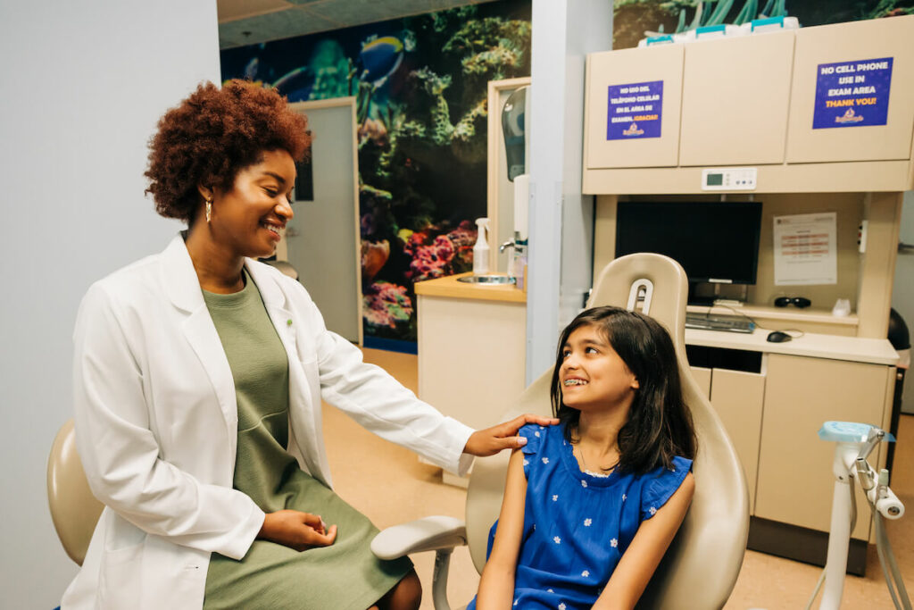 Female pediatric dentist comforting a young female patient chairside.