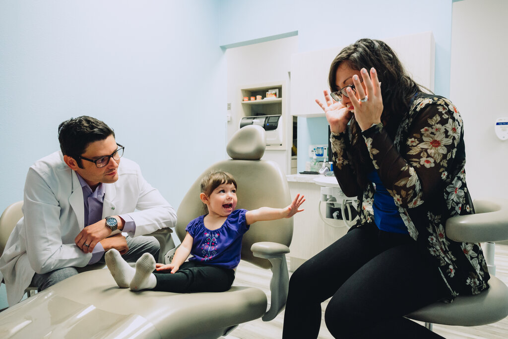 Mom playing peek-a-boo with young female patient at the dentist office.