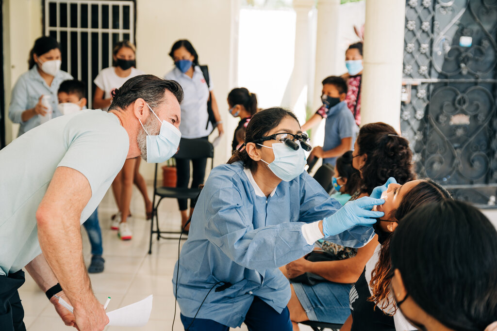 Dentist looking on and learning as another dentist works on patient.