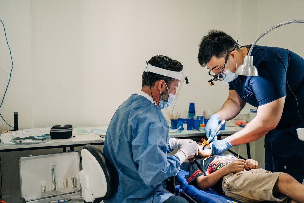 Two male dentists performing work on young child's teeth on mission trip.