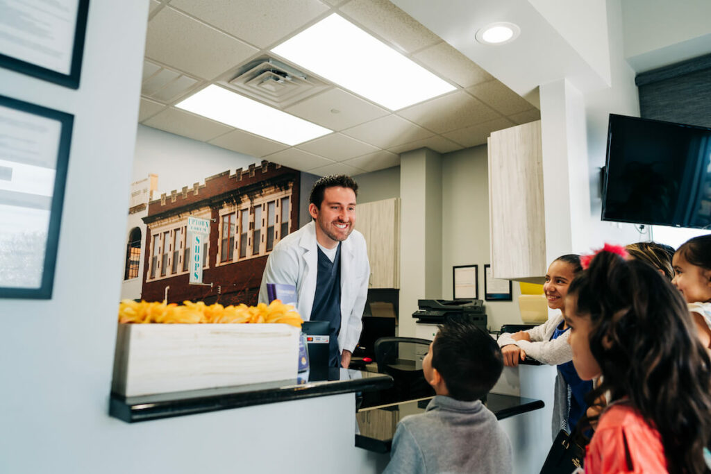 Dentist greeting small children at the front desk of a practice. 