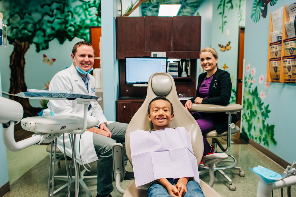 Smiling doctor, hygienist and young child in dental office setting.