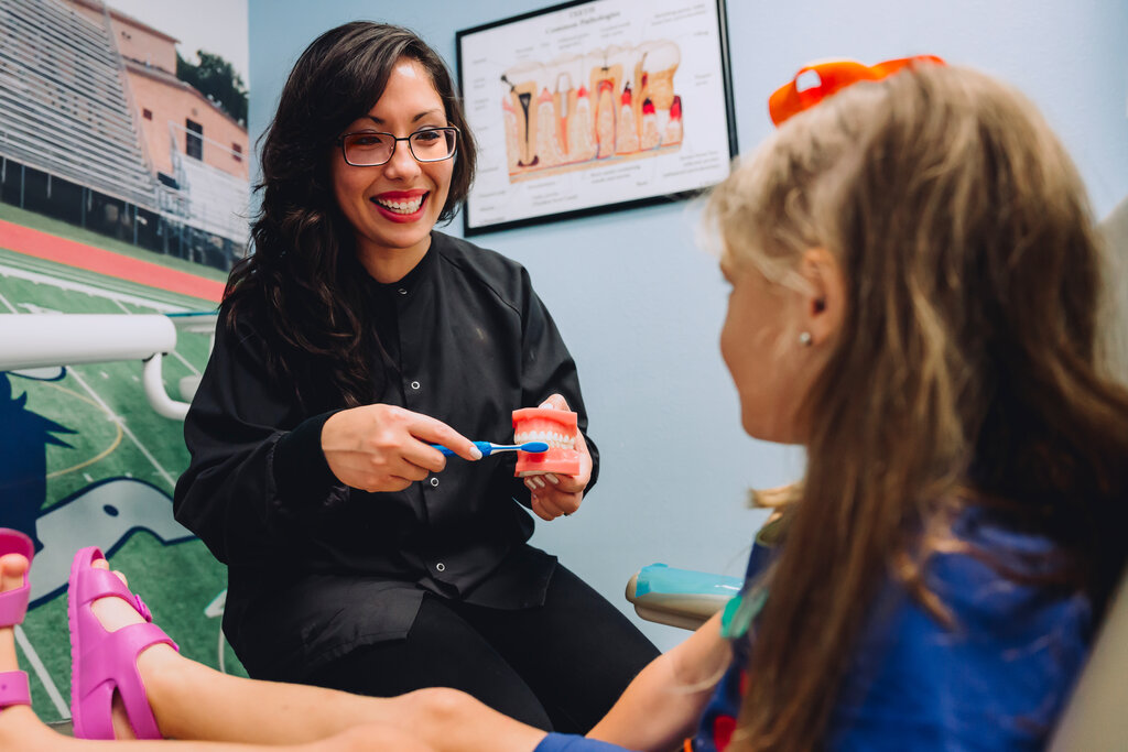 Female pediatric dentist showing young patient how to brush teeth.