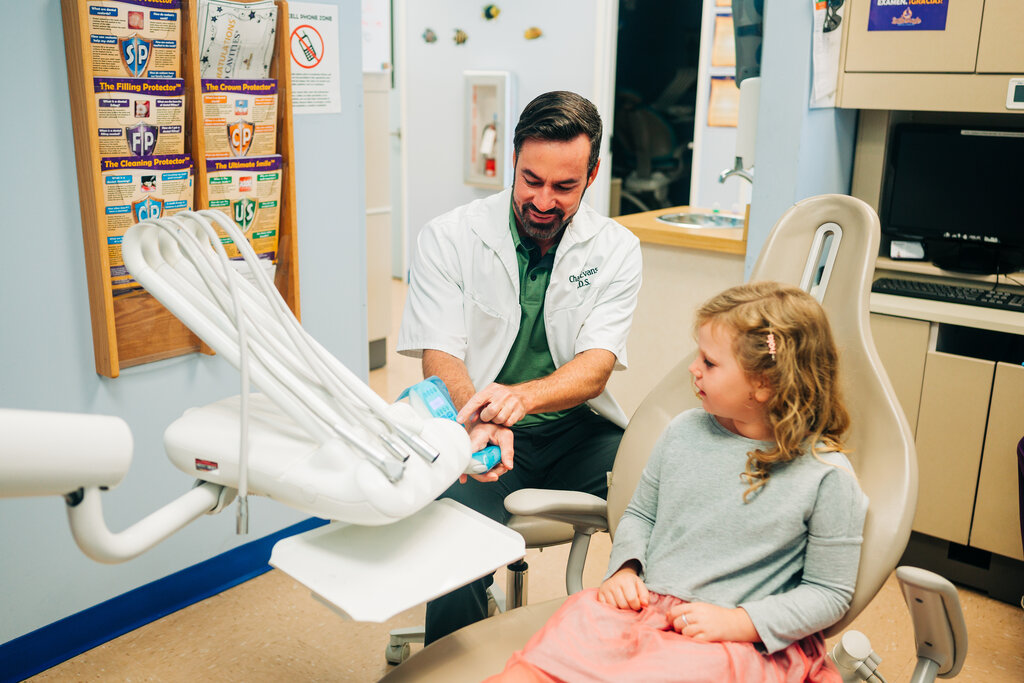 Pediatric dentist shows young patient dental tools. 