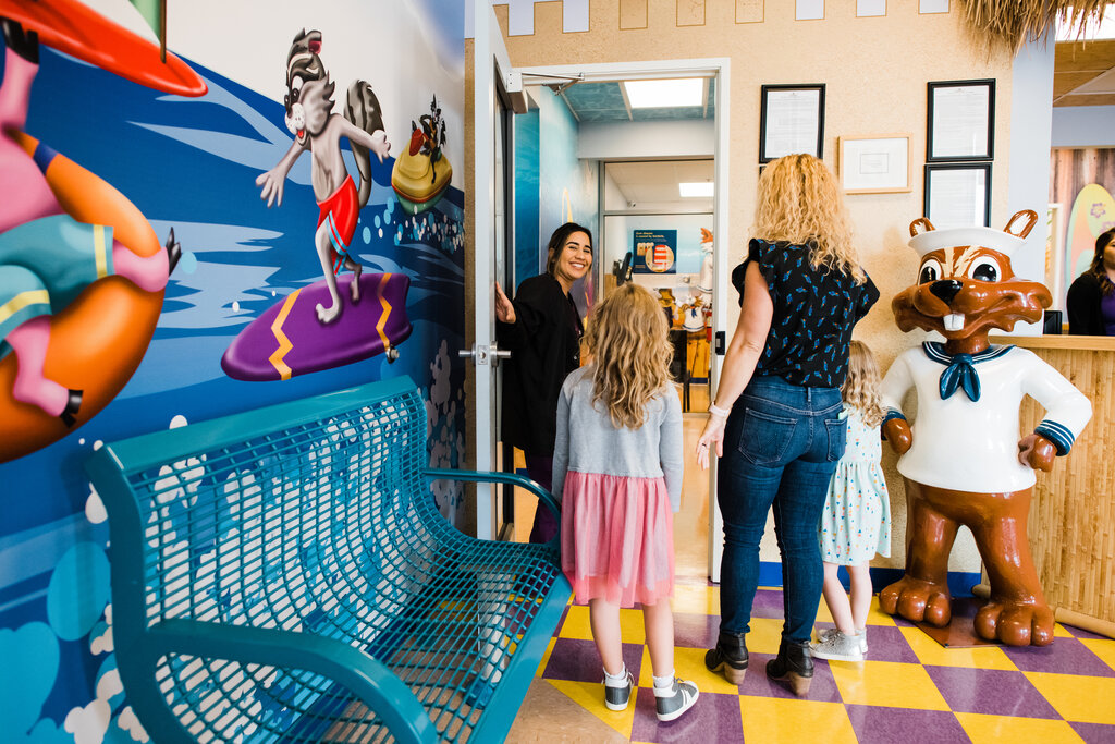 Assistant walks family back to the dental chair at a pediatric office.